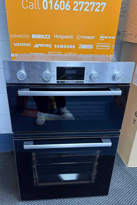 Bosch Series 2 MHA133BR0B (79) Built In Electric Double Oven in Stainless Steel from HomeWise Appliances. Showroom photo showing oven with doors closed. in front of a HomeWise sales banner.